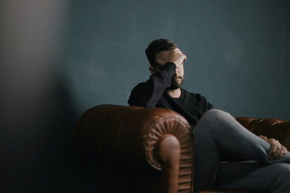 a man holds his head while sitting on a sofa